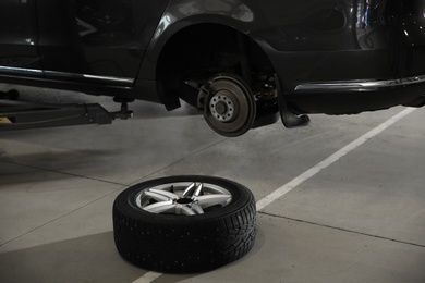 Wheel on floor near lifted car at automobile repair shop
