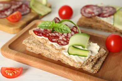 Photo of Fresh rye crispbreads with salami, cream cheese and cucumber on white wooden table, closeup
