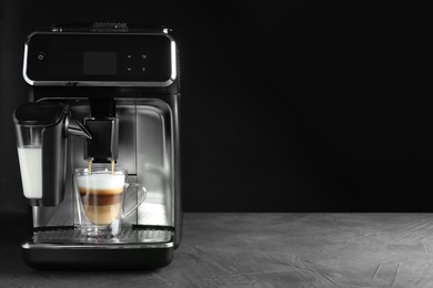 Modern coffee machine making latte into glass cup on grey table against black background. Space for text