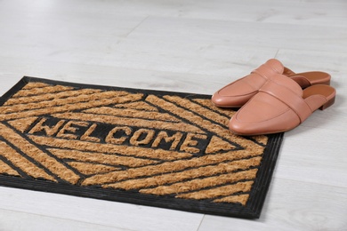 Door mat with word WELCOME and shoes on floor