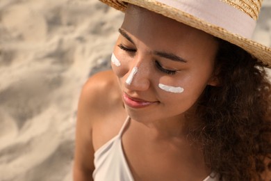 Photo of Beautiful African American woman with sun protection cream on face at sandy beach, closeup