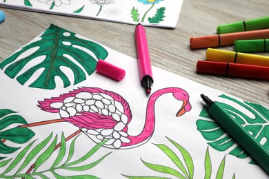 Coloring page with children drawing and set of felt tip pens on wooden table, closeup