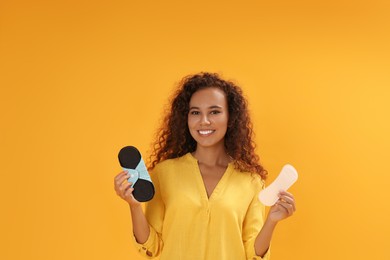 Young African American woman with reusable menstrual pad and pantyliner on yellow background.