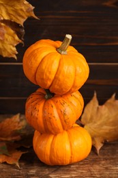 Stack of fresh ripe pumpkins and dry leaves on wooden table