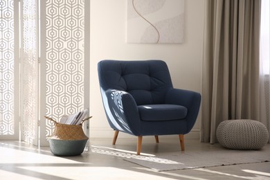 Photo of Comfortable armchair and newspaper basket in stylish room interior