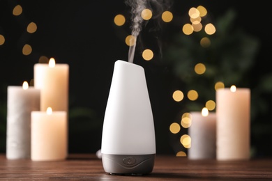 Modern aroma humidifier with candles on wooden table against blurred lights, space for text