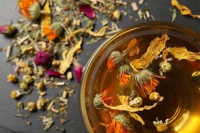 Freshly brewed tea and dried herbs on black table, top view