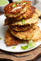 Photo of Stack of tasty parsnip cutlets with green onion on wooden board, closeup