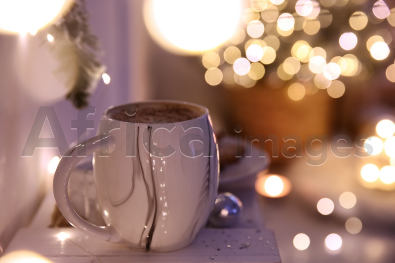 Cup of tasty hot drink against blurred Christmas lights. Space for text
