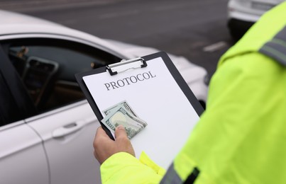 Police officer with bribe and clipboard near car outdoors, closeup