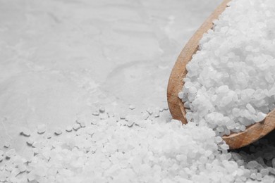 Wooden scoop and heap of natural sea salt on grey table, closeup. Space for text