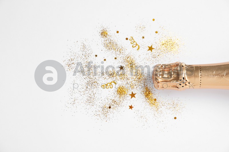 Bottle of champagne with gold glitter and confetti on white background, top view. Hilarious celebration