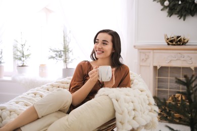 Woman with hot drink resting in comfortable papasan chair at home