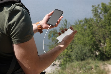 Man charging mobile phone with power bank on hill near river, closeup