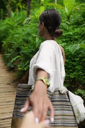Young woman holding boyfriend's hand in green tropical park