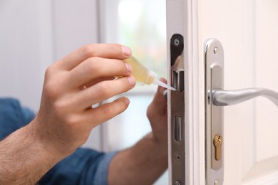 Repairman lubricating door lock at home, closeup