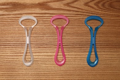 Different tongue cleaners on wooden table, flat lay