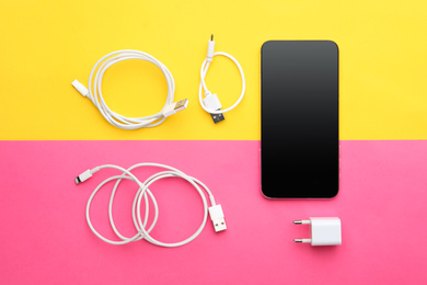 USB charge cables, power adapter and smartphone on color background, flat lay. Modern technology