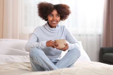 Photo of Smiling African American woman with cup of drink on bed at home