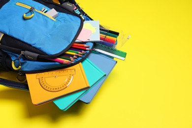 Backpack with school stationery on yellow background, space for text