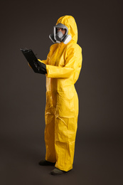 Woman in chemical protective suit holding clipboard on grey background. Virus research