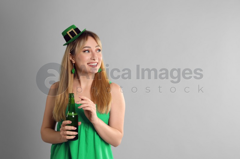 Happy woman in St Patrick's Day outfit with beer on light grey background, space for text