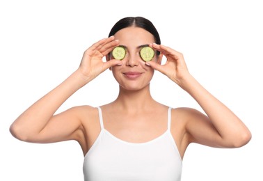 Beautiful young woman putting slices of cucumber on eyes against white background