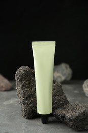 Tube of hand cream among stones on grey table against dark background. Mockup for design