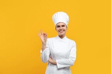 Photo of Happy female chef showing ok gesture on orange background