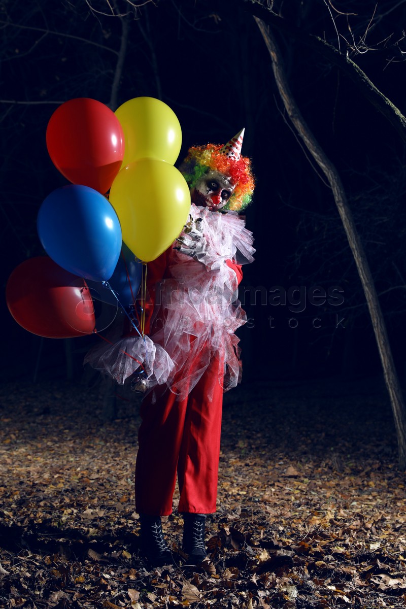 Photo of Terrifying clown with air balloons outdoors at night. Halloween party costume