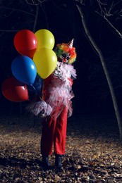 Terrifying clown with air balloons outdoors at night. Halloween party costume