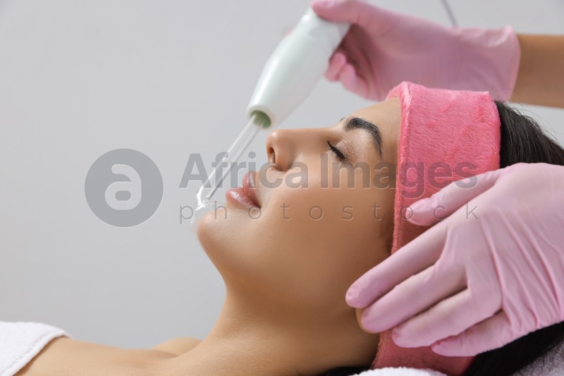 Young woman undergoing face rejuvenation procedure with darsonval in salon, closeup