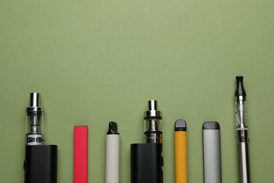 Many electronic smoking devices on olive background, flat lay. Space for text