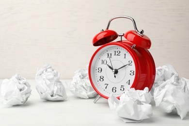 Photo of Crumpled paper balls and alarm clock on white table, space for text