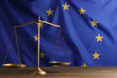 Scales of justice on wooden table against European Union flag. Space for text