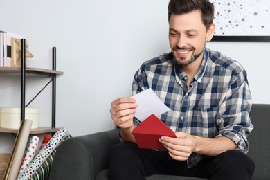 Photo of Happy man reading greeting card on sofa in living room