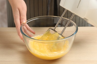 Woman beating eggs with mixer at wooden table, closeup