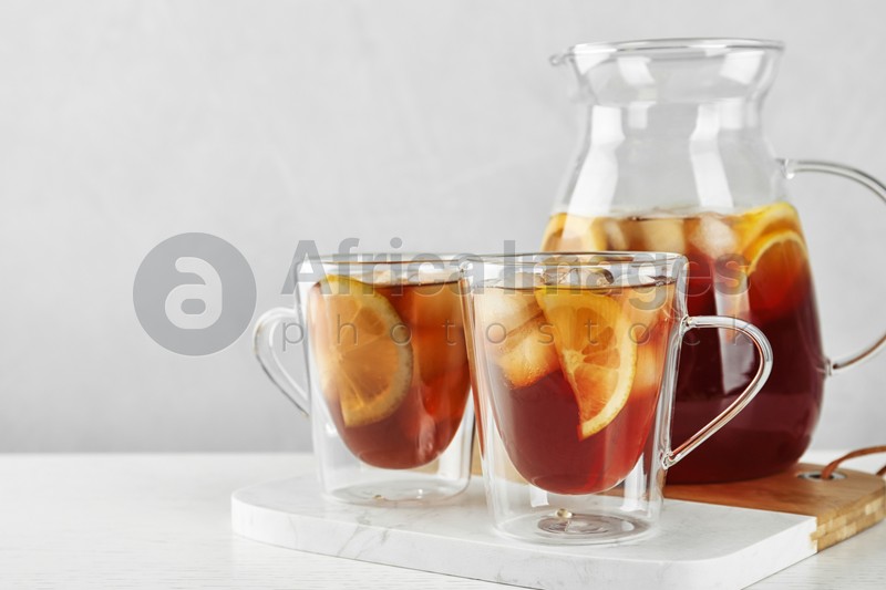 Cups and jug of refreshing iced tea on light table