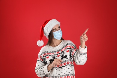 Pretty woman in Santa hat and medical mask pointing on red background