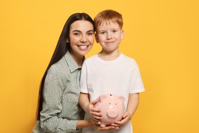 Mother and her son with ceramic piggy bank on orange background