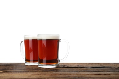 Glass mugs of delicious kvass on wooden table, white background