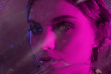 Photo of Fashionable portrait in neon lights. Beautiful young woman posing through transparent film, closeup