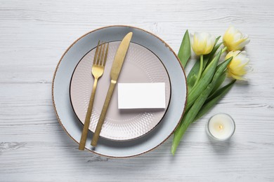 Photo of Stylish table setting with cutlery, tulips and scented candle on white wooden background, flat lay