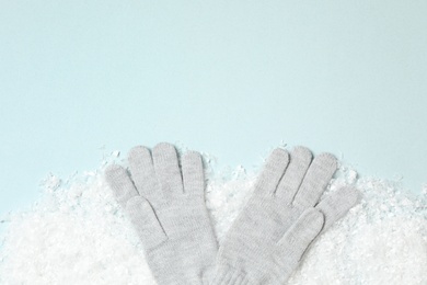 Stylish woolen gloves and artificial snow on light blue background, flat lay. Space for text