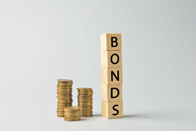 Photo of Word Bonds made of wooden cubes with letters and stacked coins on light grey background