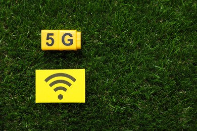 5G technology, Internet concept. Yellow cubes and card with WiFi symbol on green grass, flat lay. Space for text