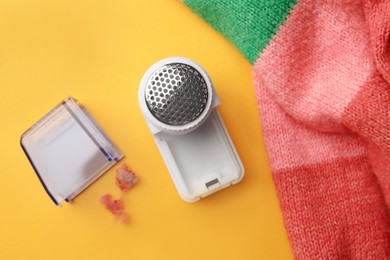 Photo of Modern fabric shaver and colorful knitted sweater on yellow background, flat lay