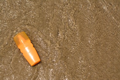 Bottle with sun protection spray on seashore, top view. Space for text
