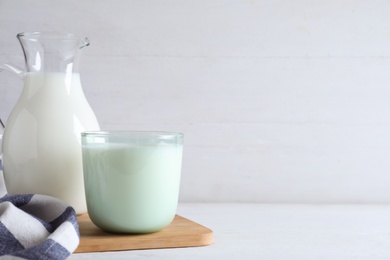 Jug and glass with fresh milk on white wooden table. Space for text