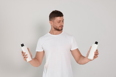 Handsome young man holding bottles of shampoo on white background